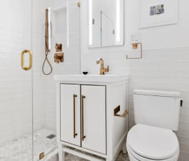 Remodeled bathroom with white tile walls and white vanity with gold fixtures and accents.