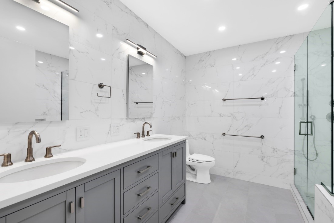 Remodeled bathroom with white tile walls and double vanity with gray cabinets.