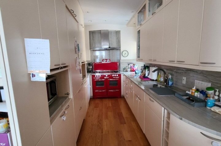 Remodeled galley kitchen with white cabinets and gray stone countertops, and red gas stove.