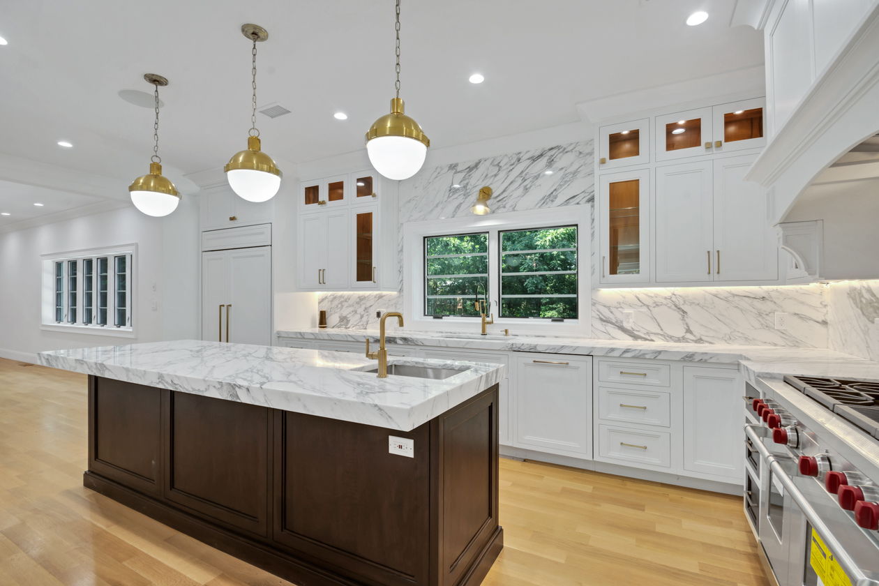 Remodeled kitchen with white marble counters, large island, pendant lighting, and white cabinets.