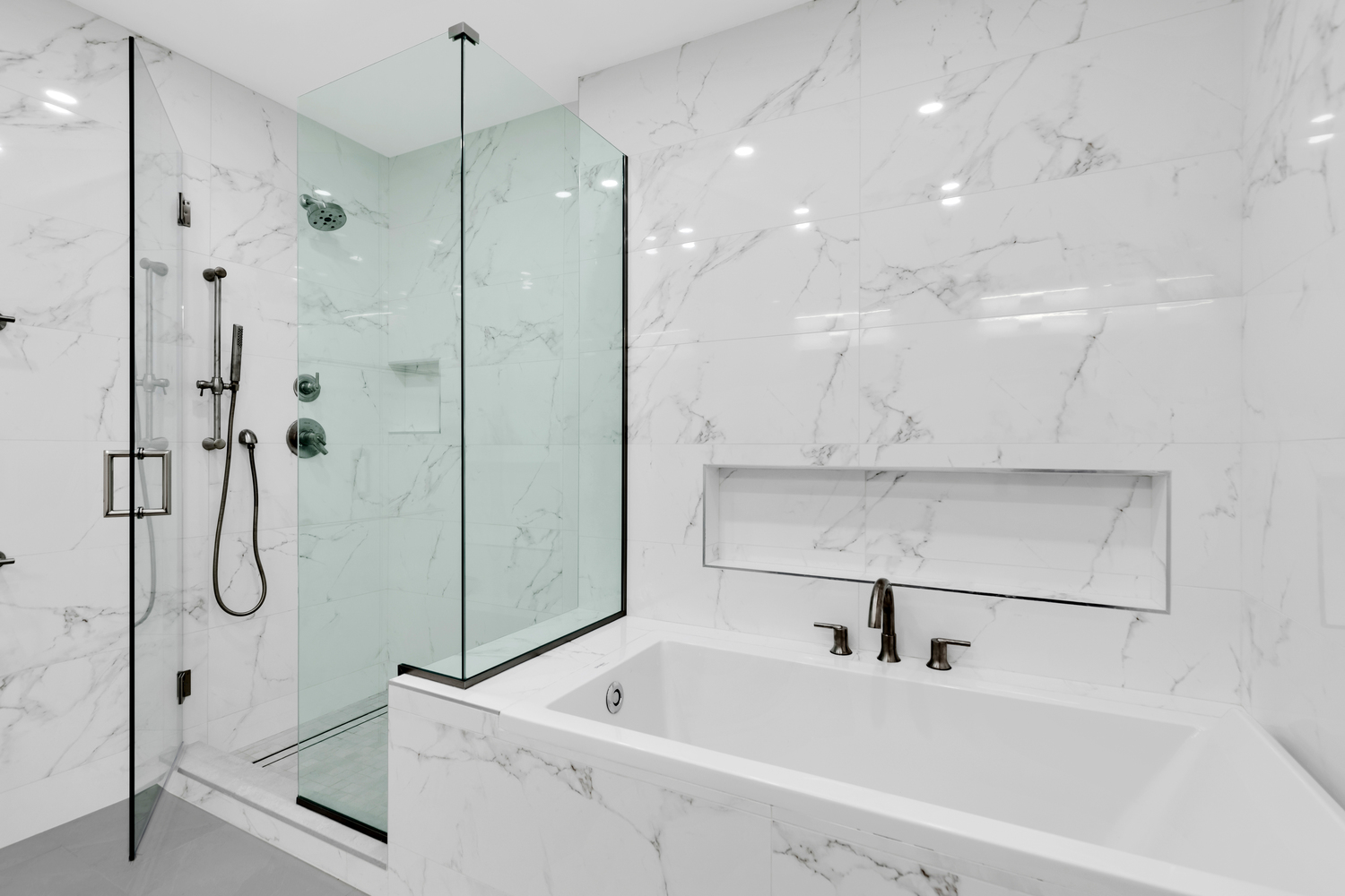 Remodeled bathroom with white tile walls, glass enclosed shower, and separate large tub.