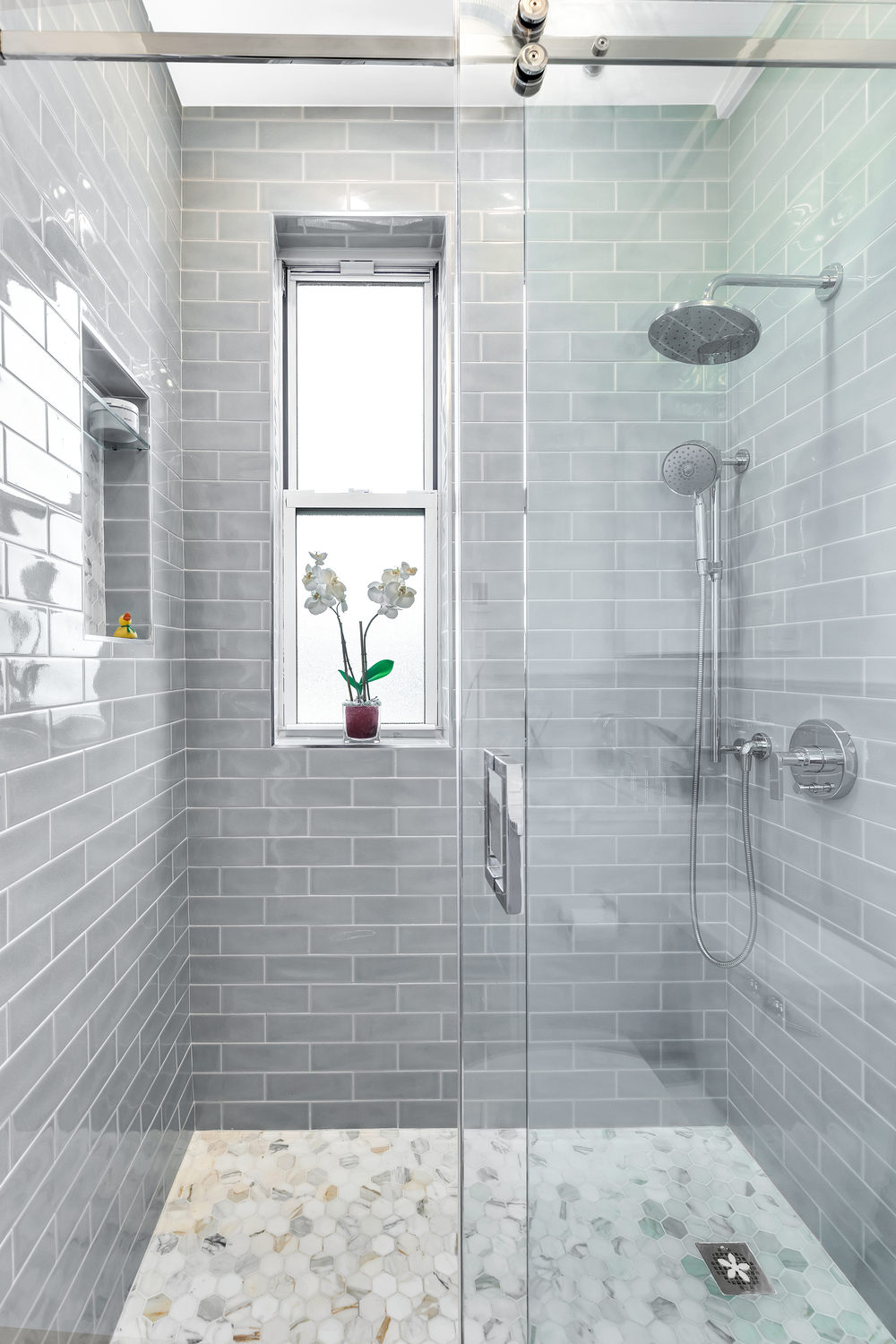 Remodeled bathroom with glass shower and gray tiles