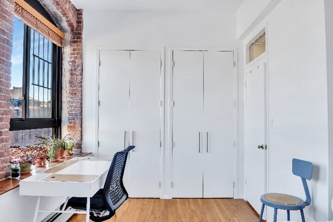 remodeled room with one brick wall, wood floors, and two side-by-side closets on white wall.