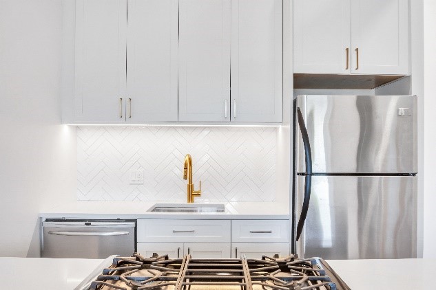 Remodeled kitchen with white cabinets, stainless steel appliances, and gold modern faucet.