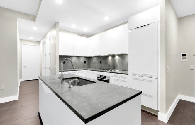 Remodeled kitchen with white cabinetry, large kitchen island with black countertop, and recessed lighting